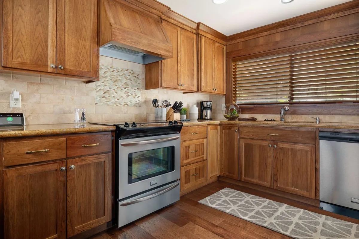 A well-appointed kitchen nook featuring a stainless steel stove, granite countertops, wooden cabinets, and a cozy kitchen rug. The space is designed for cooking, entertaining, and family gatherings, seamlessly flowing into the living and dining areas.