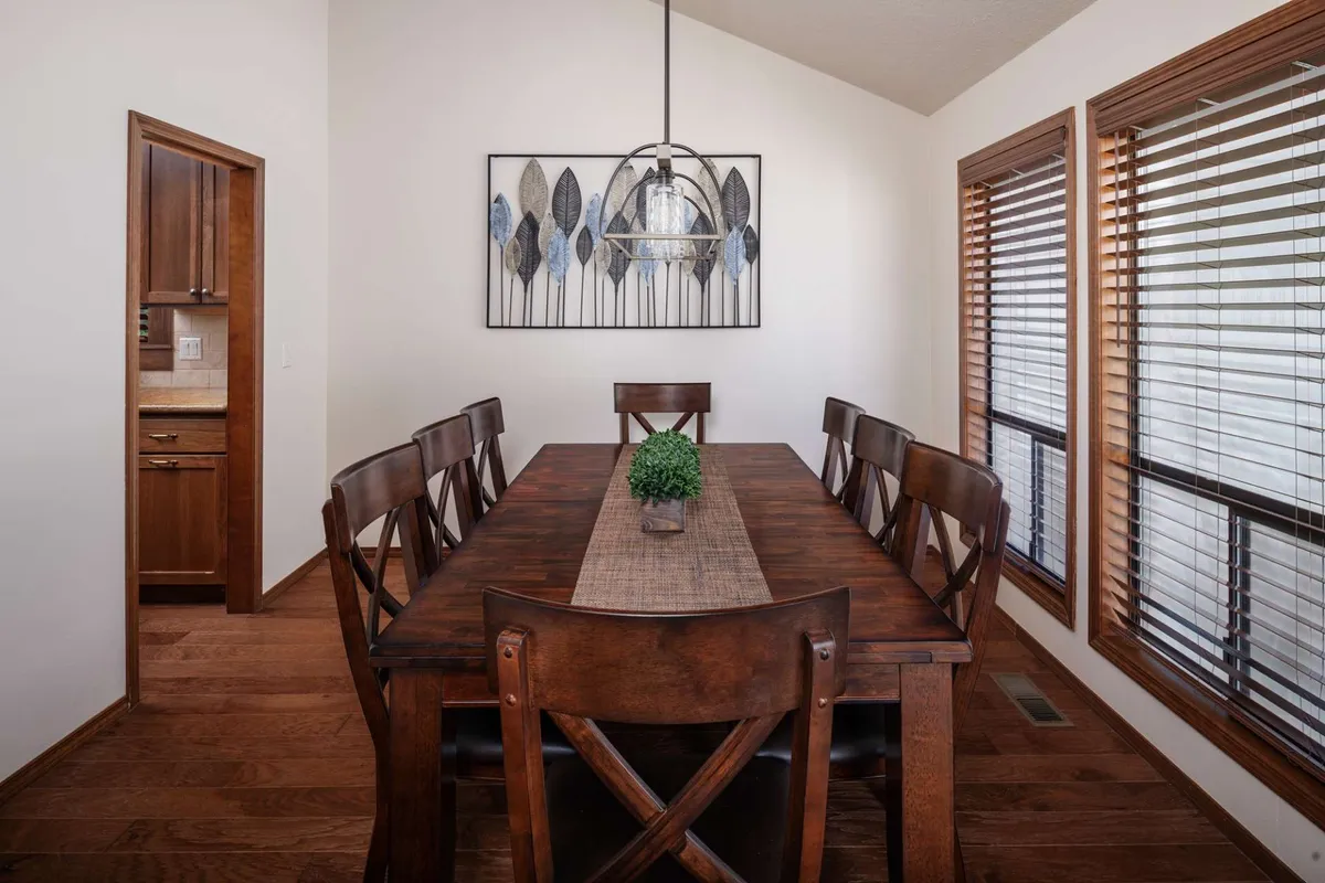 A warm dining space with a large table under a dazzling chandelier, surrounded by wall art and large windows letting in ample natural light. The setting is ideal for family dinners, entertaining guests, or celebrating holidays, with a welcoming and festive ambiance.