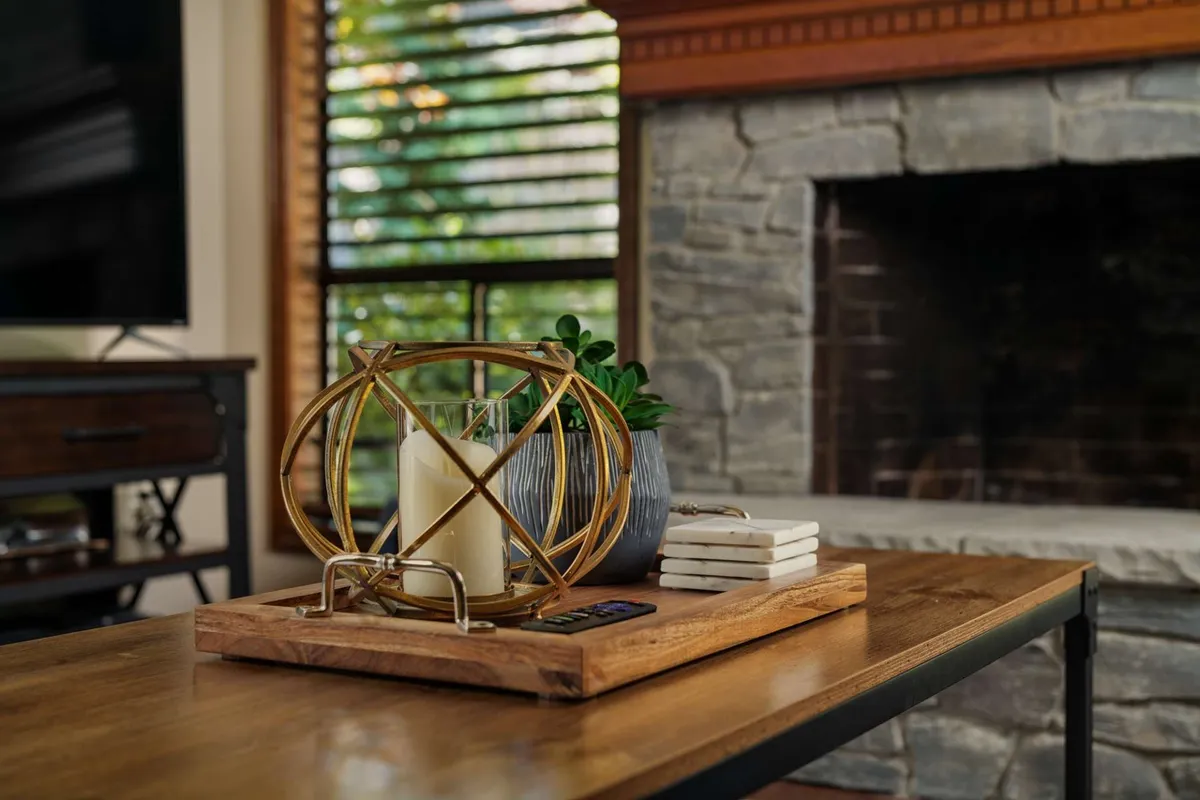 A cozy living area featuring a stylish stone fireplace, decorative wooden sphere, candles, and a lush succulent plant. The space looks warm and inviting, with comfortable furnishings arranged for social gatherings.