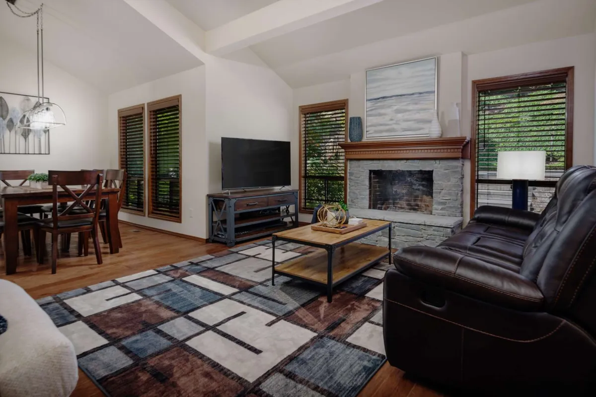 The image showcases a warm and inviting open-concept living and dining area, featuring a crackling fireplace, a plush sofa perfect for movie nights, a stylish rug, and a spacious dining table ready for shared meals and heartfelt conversations. The space is bathed in soft natural light, emphasizing comfort and togetherness.